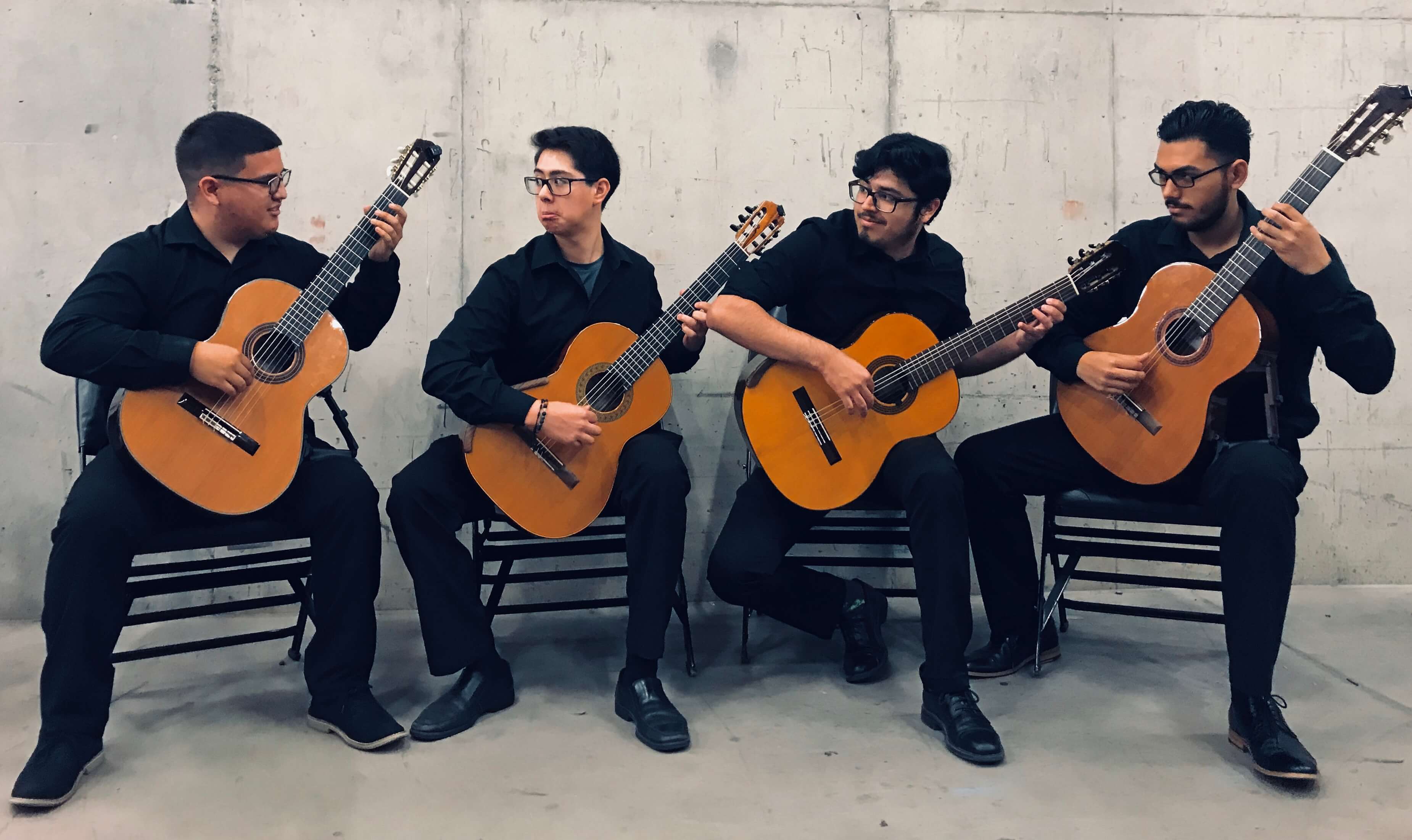Four students sitting down playing their guitars in a concert