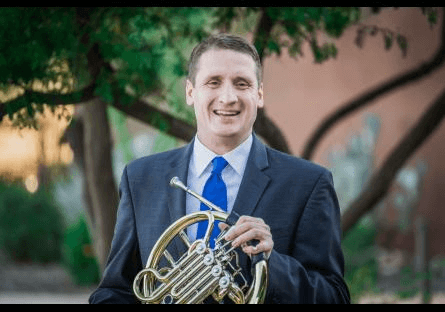 Alex Manners in a suit smiling and holding his instrument.