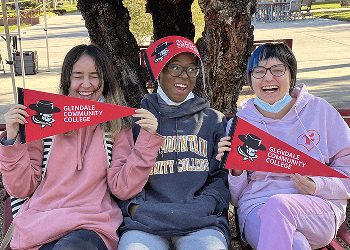 Three Students sitting on the campus lawn holding Gaucho pennant banners