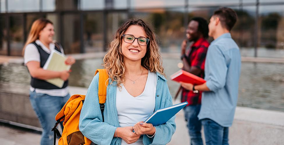 Smiling student carrying a blue notebook and yellow backpack