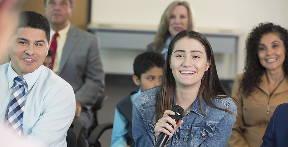 Smiling female student answering questions at a Town Hall meeting.