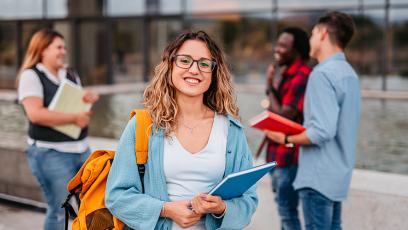 Smiling student carrying a blue notebook and yellow backpack