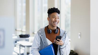 Male college student in lecture room, smiling and using a smartphone.