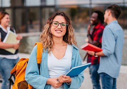 Smiling student carrying a blue notebook and yellow backpack