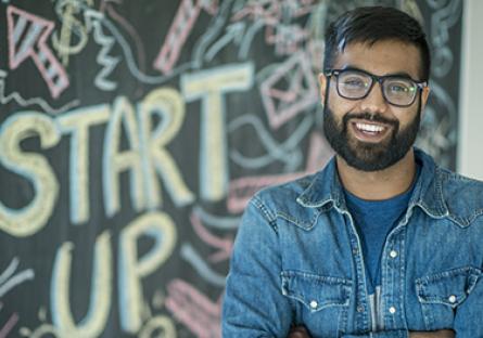 An entrepreneur standing in front of a black board with the words "start up"
