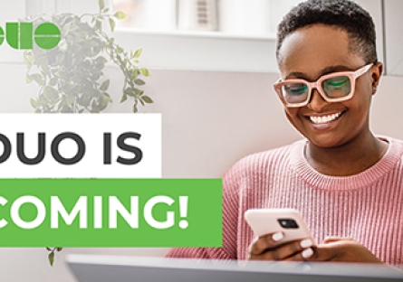 Female student sitting at a laptop and using a phone with the words "DUO is Coming!"