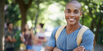 Smiling male student in a blue shirt with students standing in the background.
