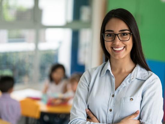 A teacher smiling with students at their desks in the background.