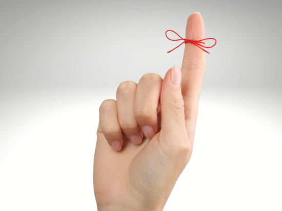 Woman showing index finger with tied red bow as reminder on light grey background