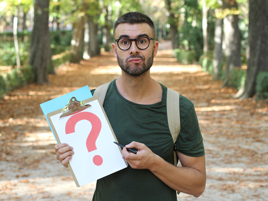 Indecisive male student holding a clip board with a red question mark.