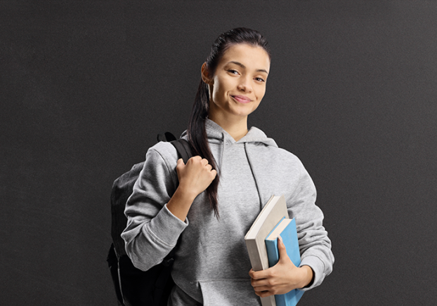 Smiling female student wearing a gray hoodie and black backpack and holding textbooks.
