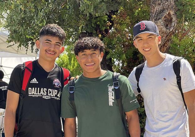 Three students standing on campus lawn smiling