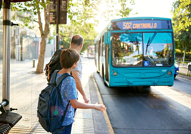 Man and young son standing at bus stop as vehicle approaches.
