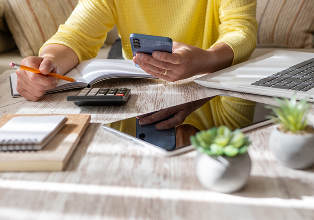 Woman in a yellow shirt using a smartphone and calculator.