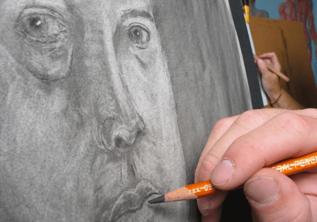 An art student sketching a persons face in a graphite medium