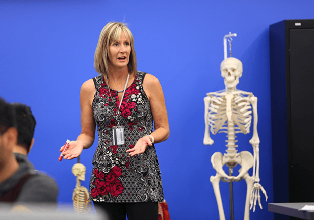 Biology teacher lecturing in front of a skelton.